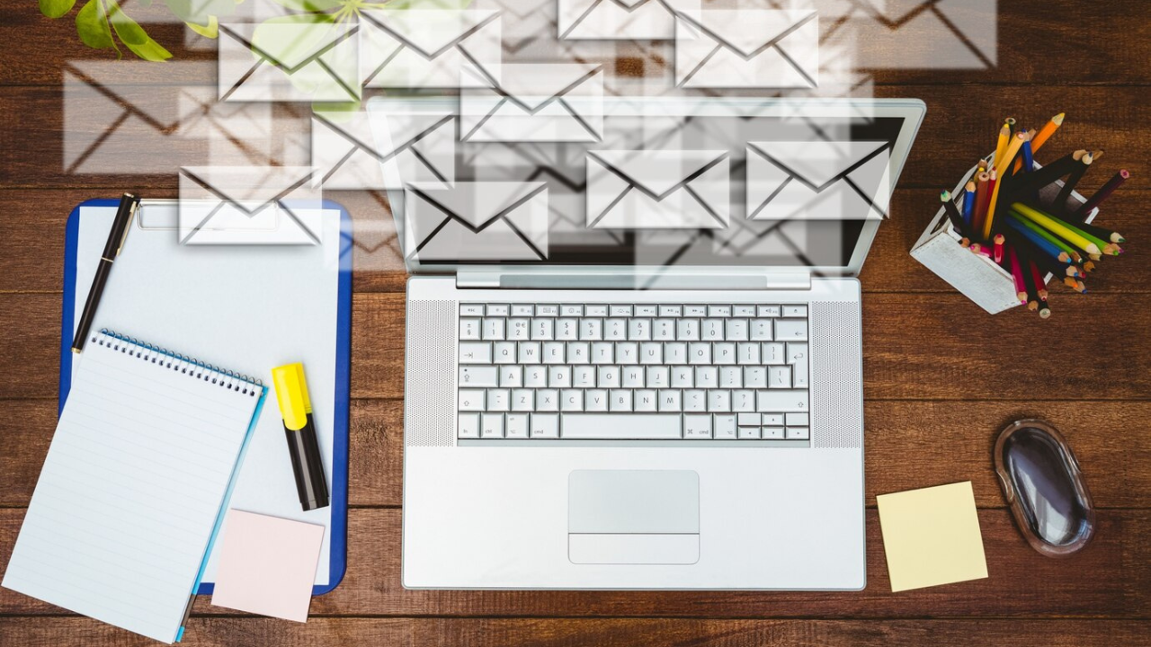 Laptop on a wooden desk with digital envelopes emanating from the screen, representing email marketing.
